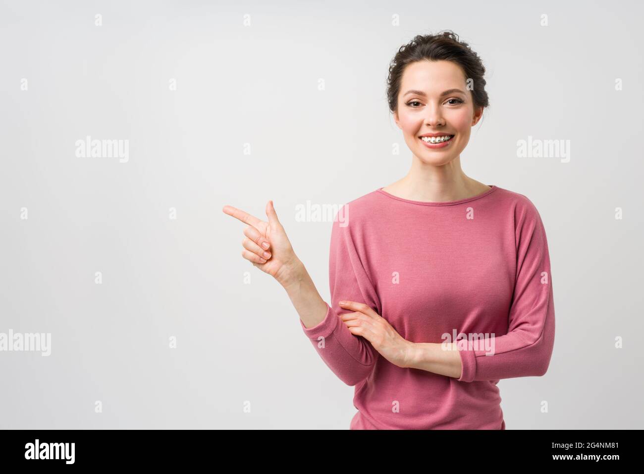 A young woman with braces on her teeth, smiles and points to the copy space with a hand gesture Stock Photo