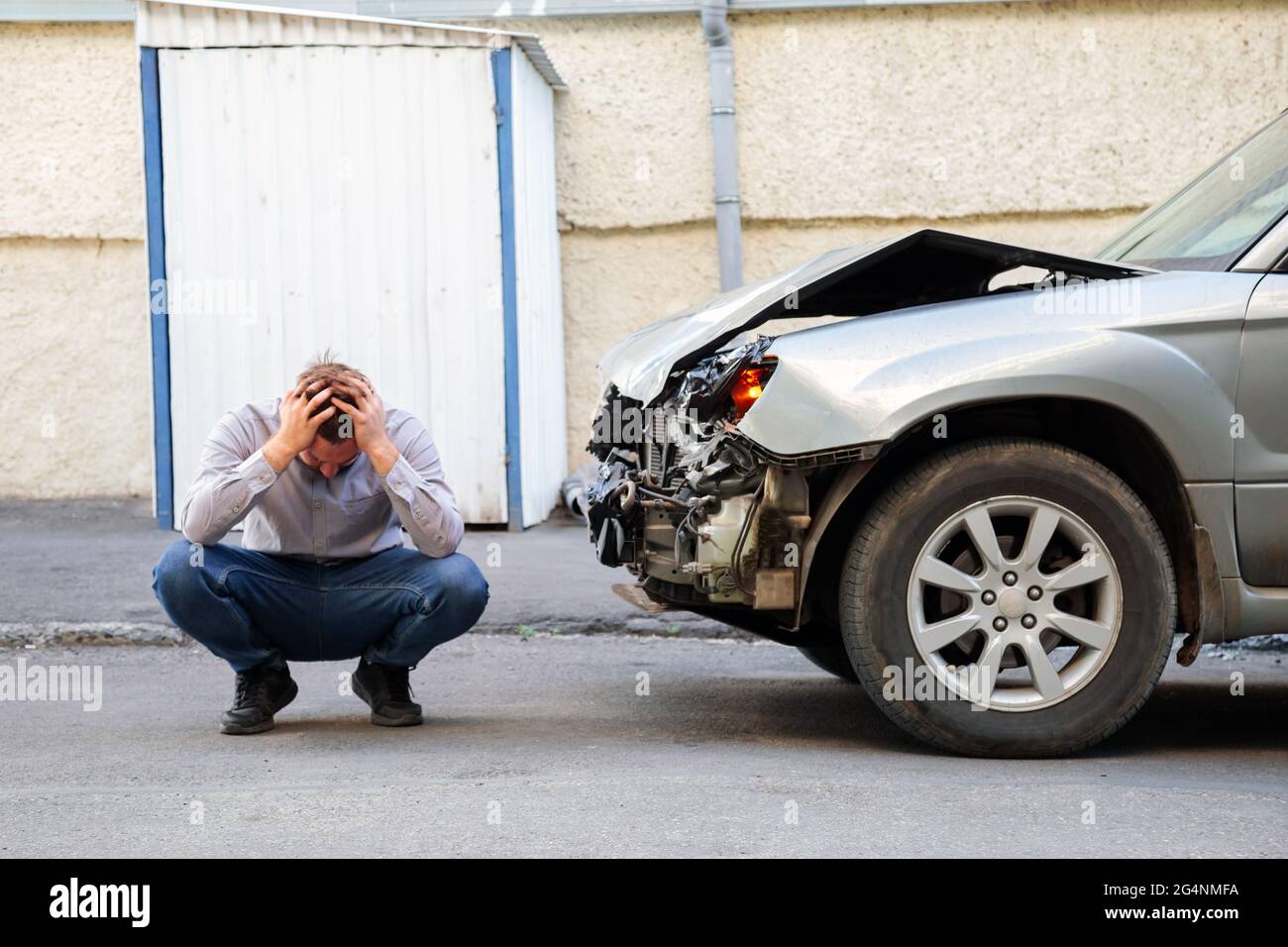 Young man driver in car accident holding his head near broken car on the road after car accident. Caucasian man facepalm holding head injury after Stock Photo