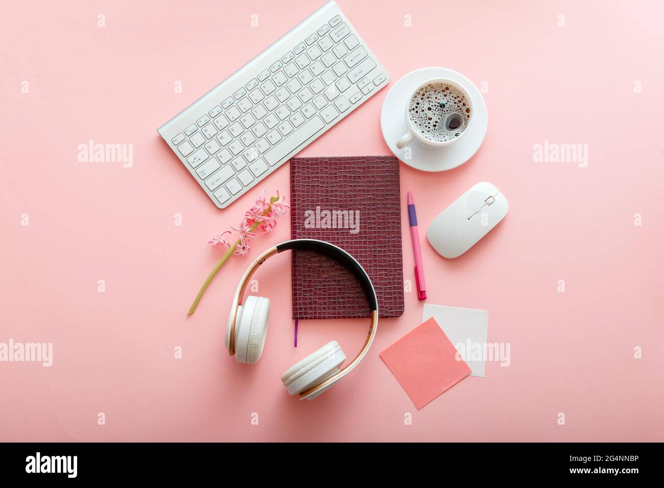 Office supplies on color pink table work desk. Girly workspace with keyboard mouse notepad headphones and coffee flower. School girl student workplace Stock Photo