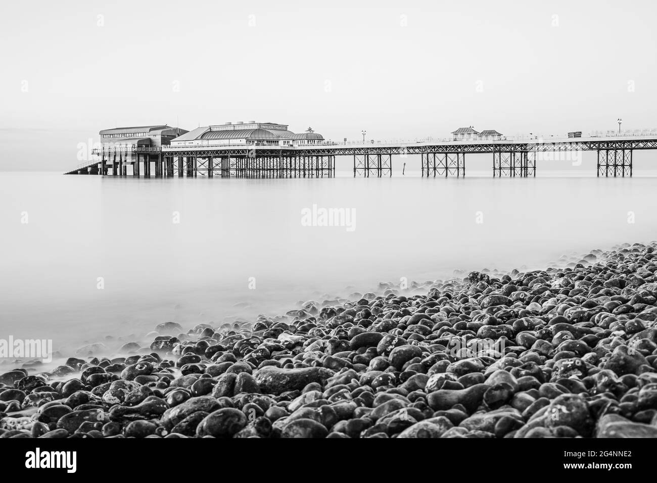 Cromer pier seen over the pebble beach in a long exposure taken in June 2021 on the North Norfolk coast. Stock Photo