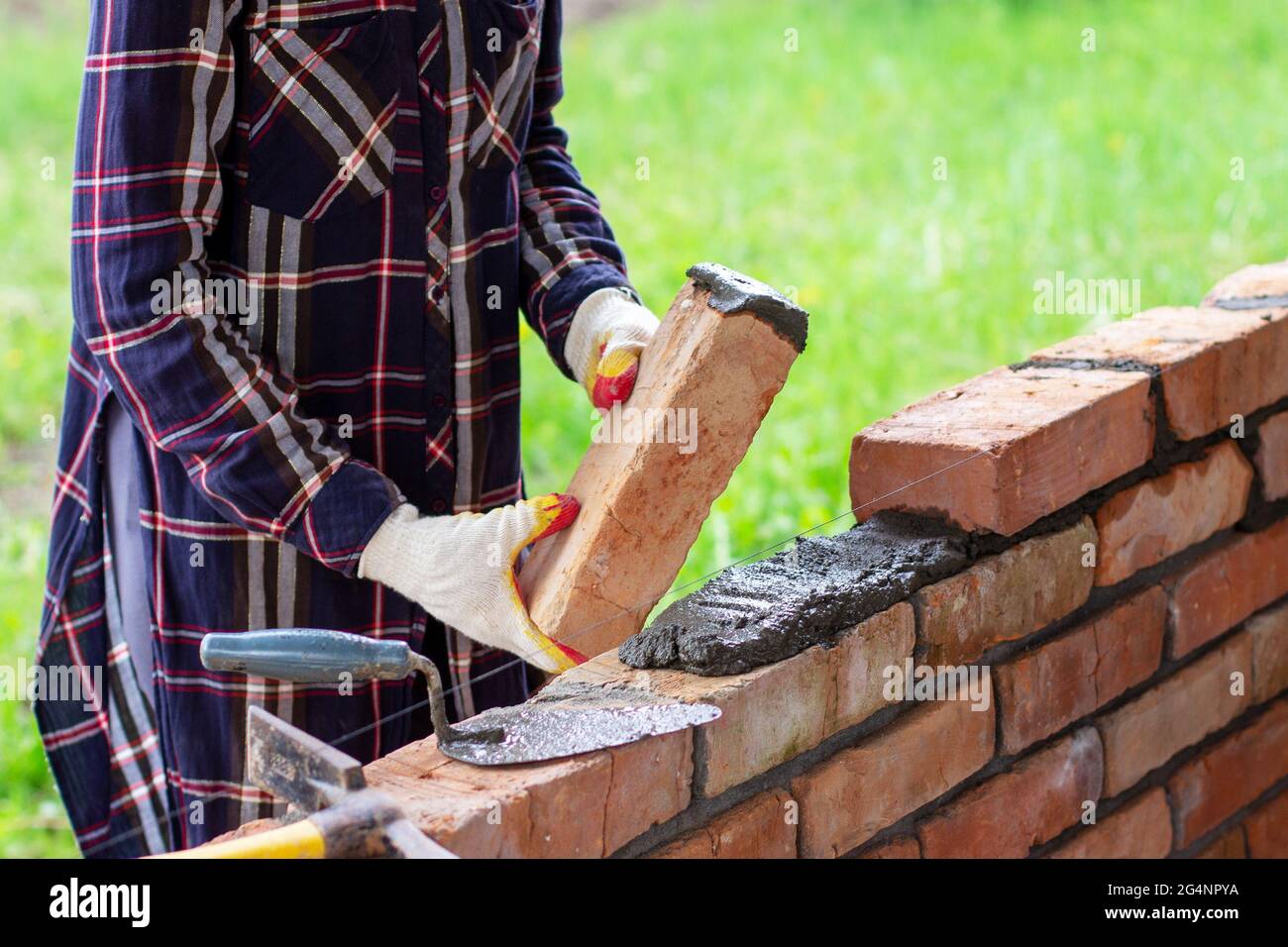 a young woman builds a brick wall, puts a brick on a cementsand mortar