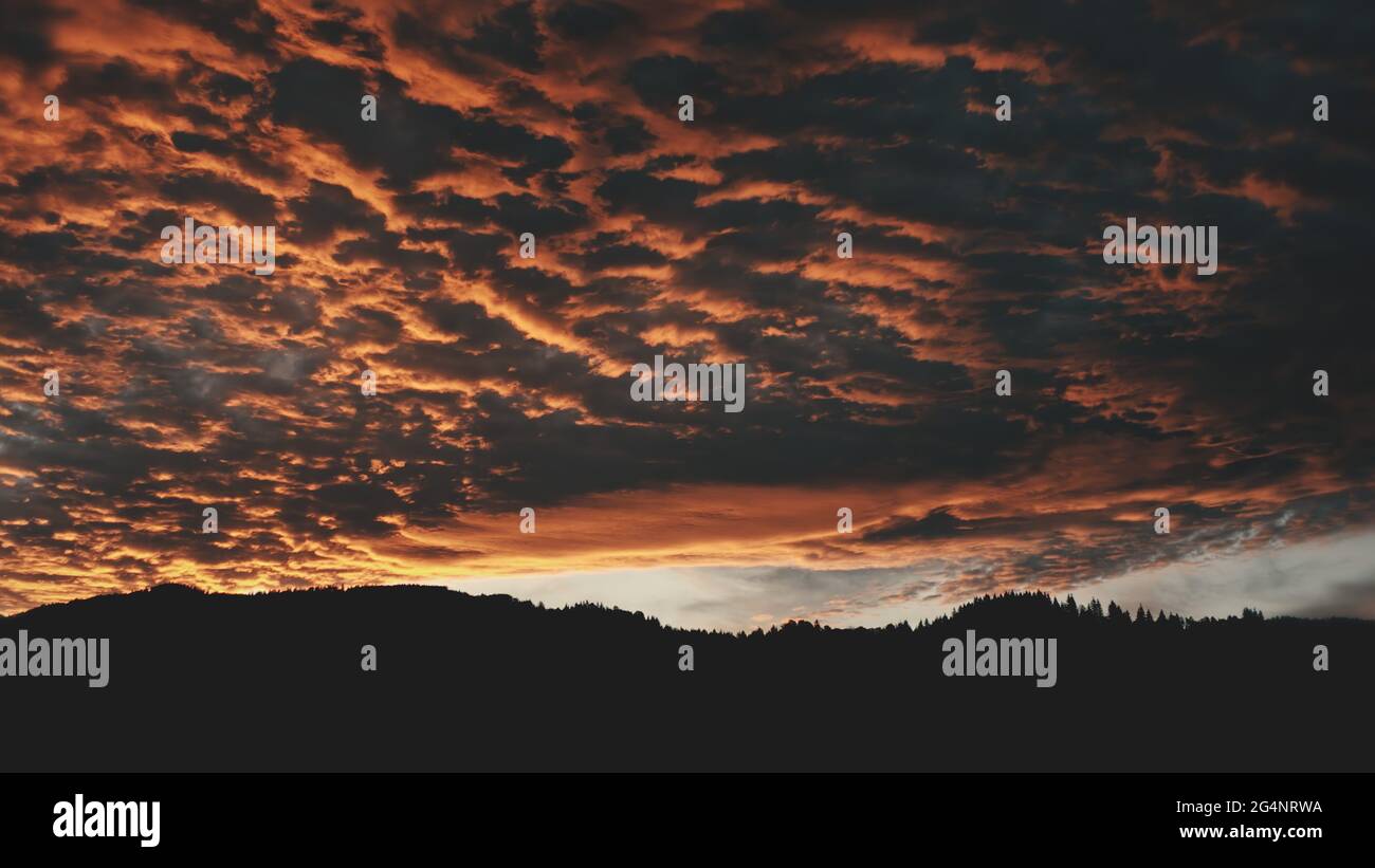 Dark sunset over mountain range silhouette aerial. Sun set above wild nature landscape. Dramatic colorful sky with heavy cumulus clouds. Spruce trees forest on mounts top, hills. Cinematic drone shot Stock Photo