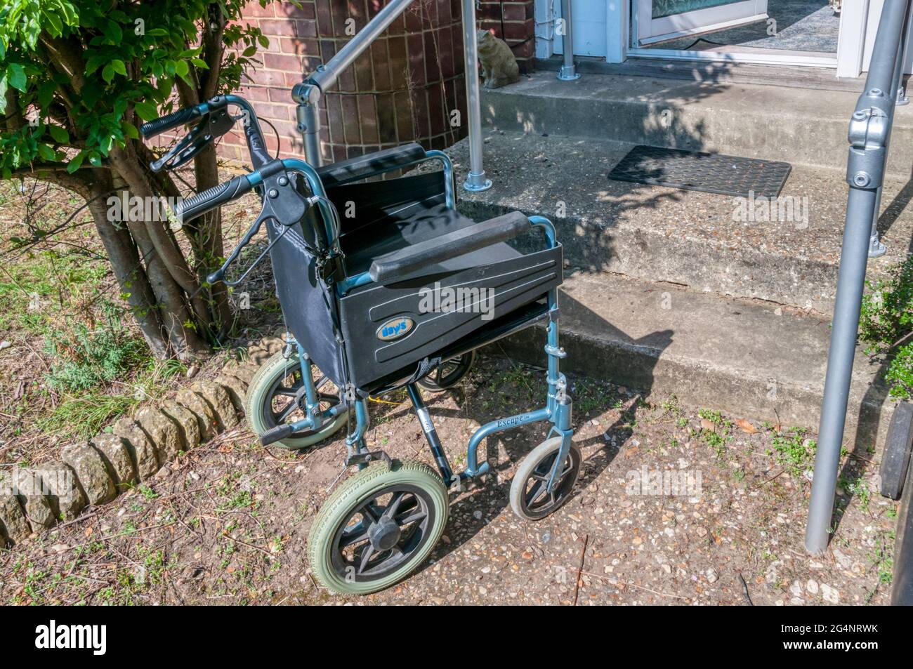 An empty wheelchair at the bottom of steps leading up into a house. Stock Photo