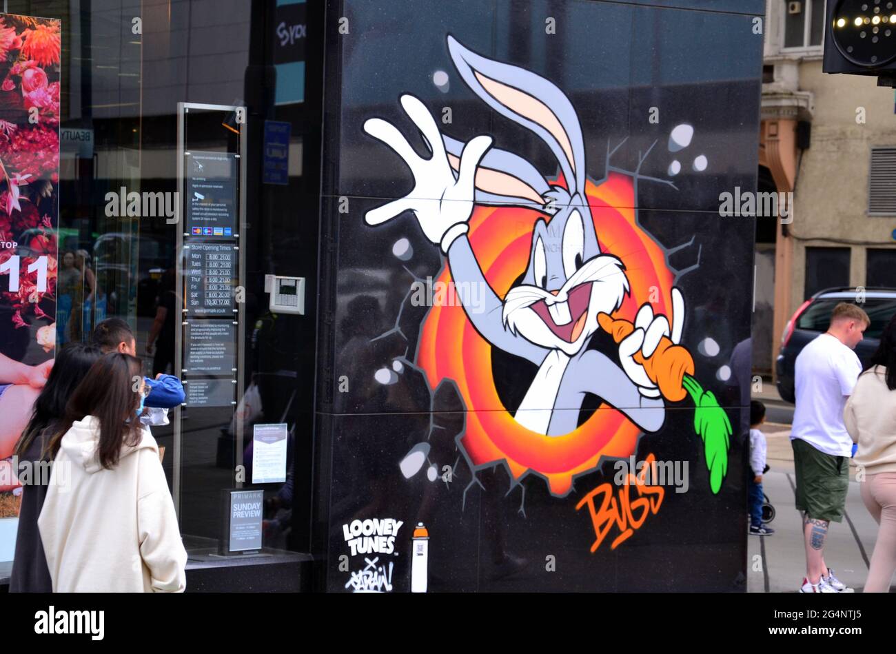Passers - by near a Bugs Bunny image, part of a Looney Tunes art trail which has opened in Manchester, England, United Kingdom. The trail will mark the film Space Jam: A New Legacy which will be in cinemas in Manchester soon. The cartoon images appear in 12 locations in Manchester. Stock Photo