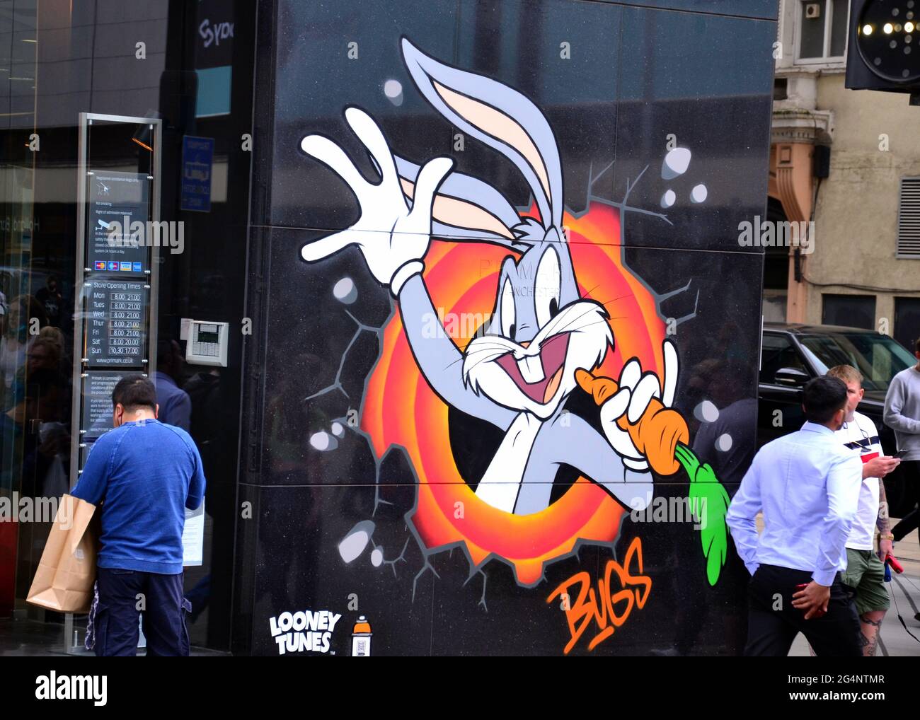 Passers - by near a Bugs Bunny image, part of a Looney Tunes art trail which has opened in Manchester, England, United Kingdom. The trail will mark the film Space Jam: A New Legacy which will be in cinemas in Manchester soon. The cartoon images appear in 12 locations in Manchester. Stock Photo