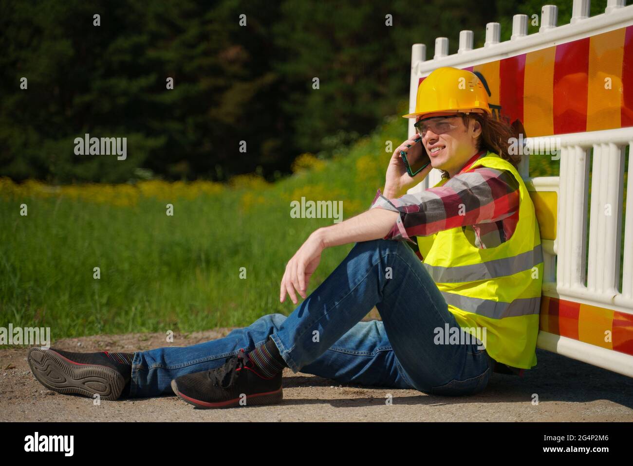 Male worker in hardhat and high vis jacket using smartphone. Stock Photo