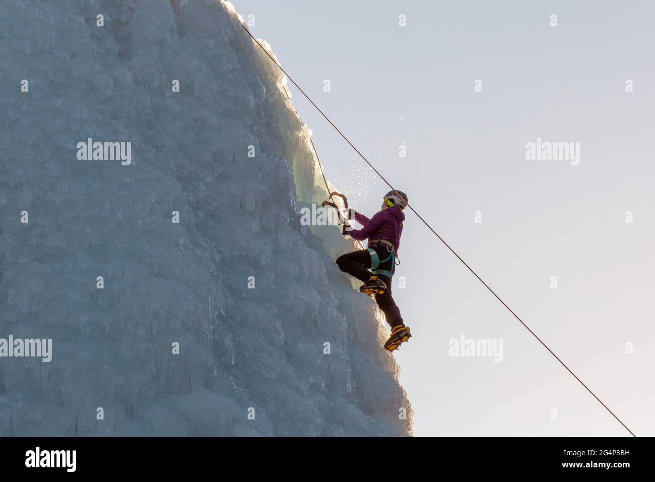 Female ice climber hiking a frozen waterfall, pushing axe pick into the ...