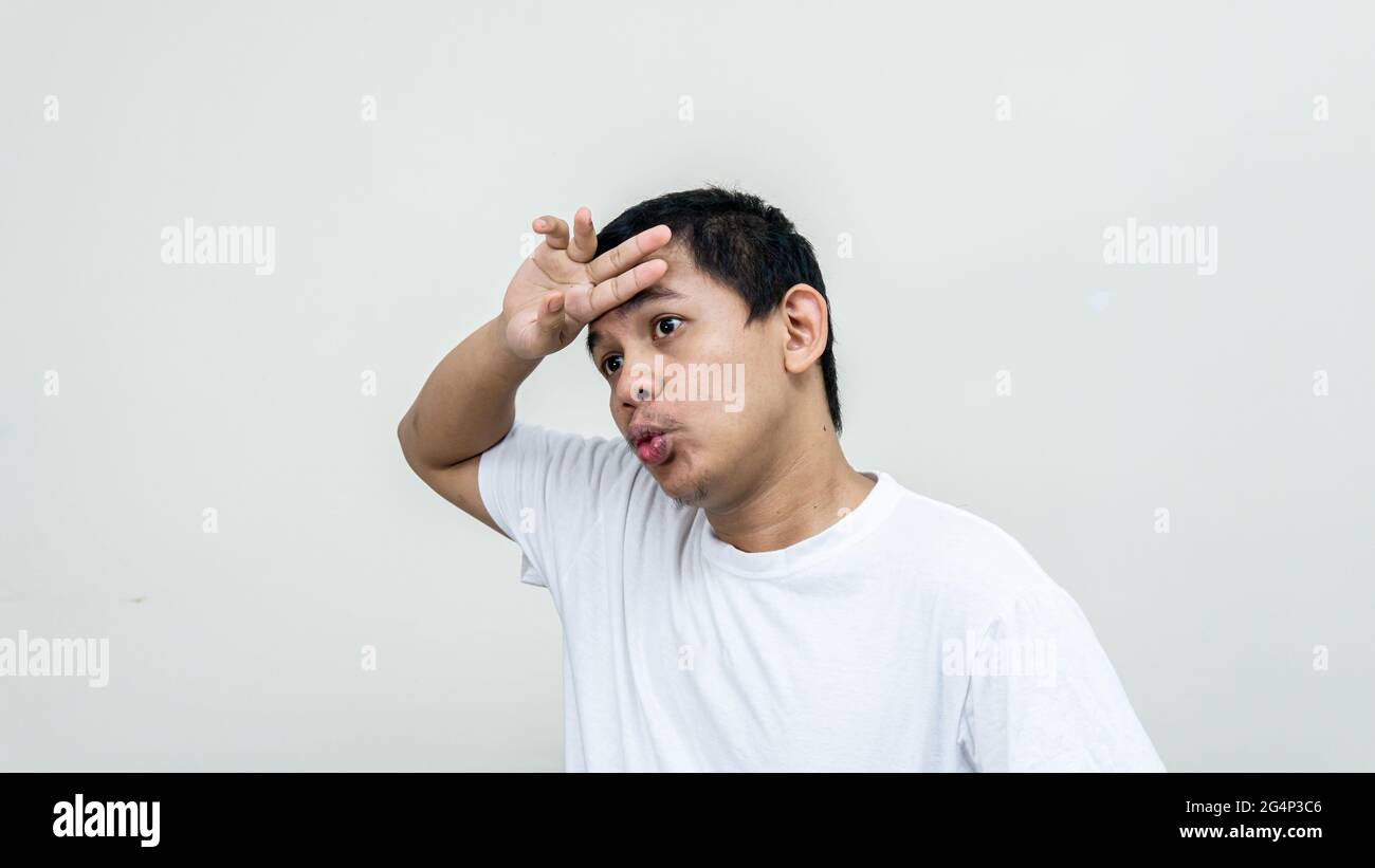 Malay man feeling relieved while wiping the sweat on the forehead and exhaling on a white background Stock Photo