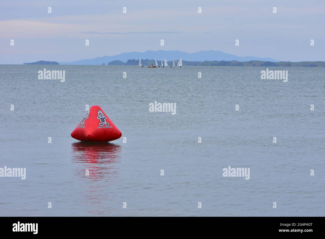 Red inflatable float on calm sea surface with sailing dinghies and support vessel in blurred background. Stock Photo
