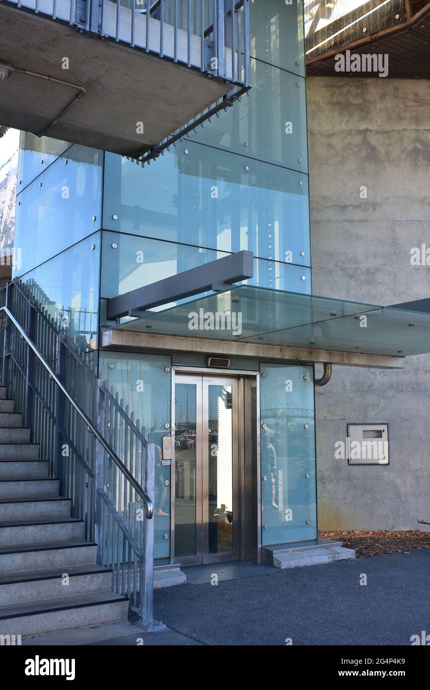Public lift shaft with transparent glass walls and concrete staircase leading to pedestrian bridge over motorway. Stock Photo