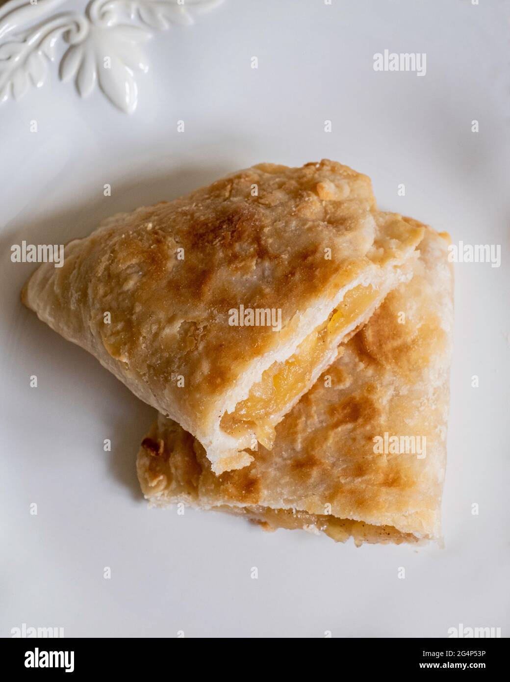 Homemade fried apple pie cut in half made from dried apples with flaky pie crust on a white plate. Stock Photo