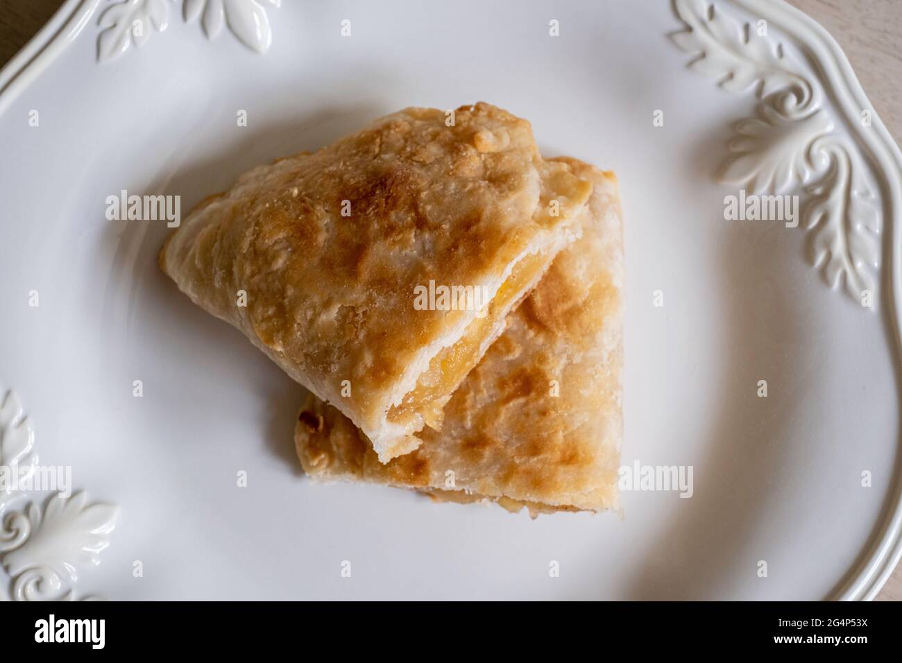 Homemade fried apple pie cut in half made from dried apples with flaky pie crust on a white plate. Stock Photo