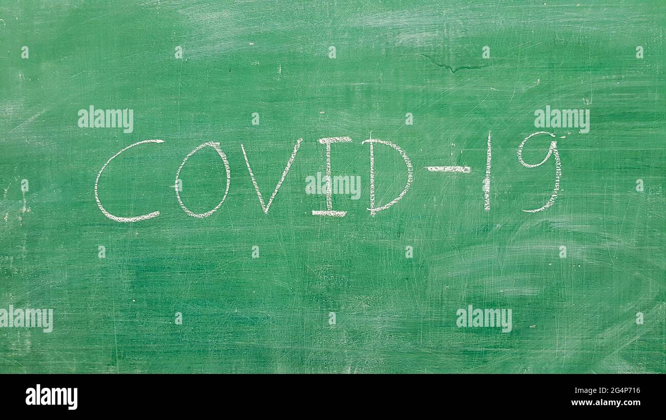 Covid-19 word written on green board with white chalk in classroom Stock Photo