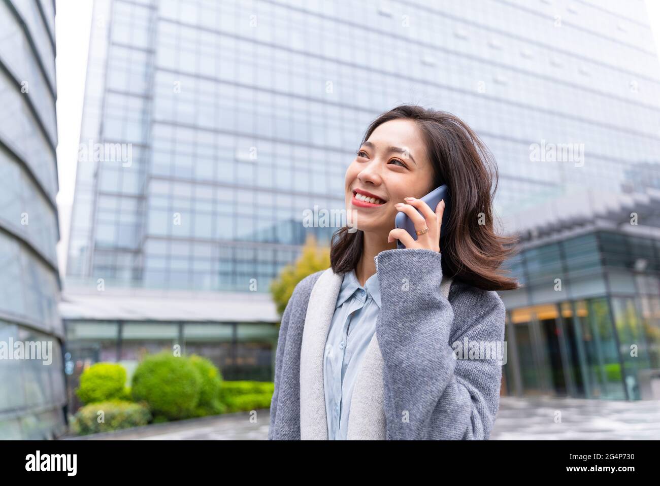 Young beautiful girl walking outside office building using mobile phone and happily calling customers Stock Photo