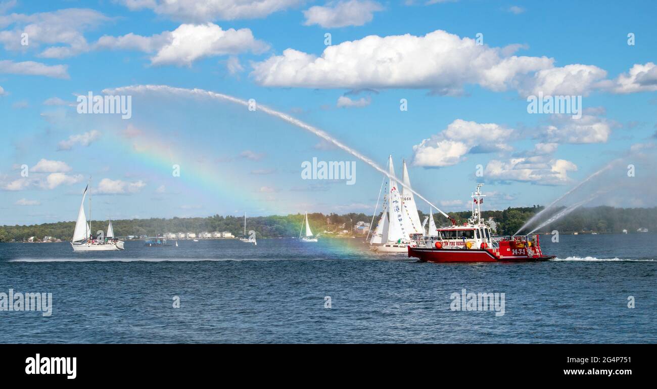 Firefighting ship demonstrating its reach and creating a rainbow. Sunny day on the water with white fluffy clouds in a bright blue sky. Stock Photo