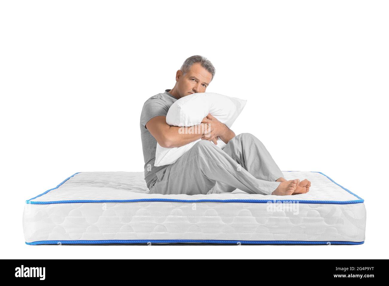 Sad mature man sitting on soft mattress against white background Stock