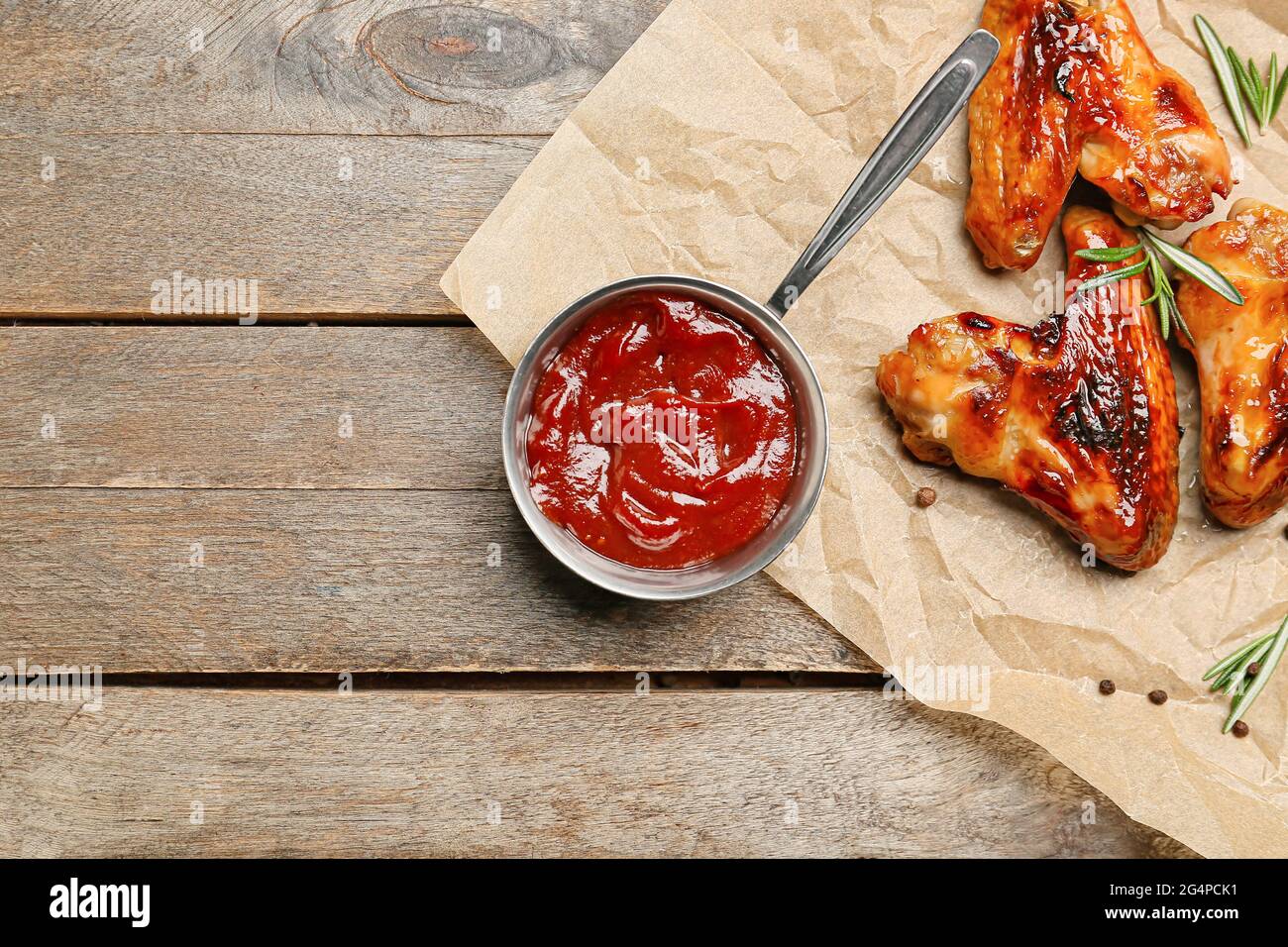 Chicken wings and pot with barbecue sauce on wooden background Stock