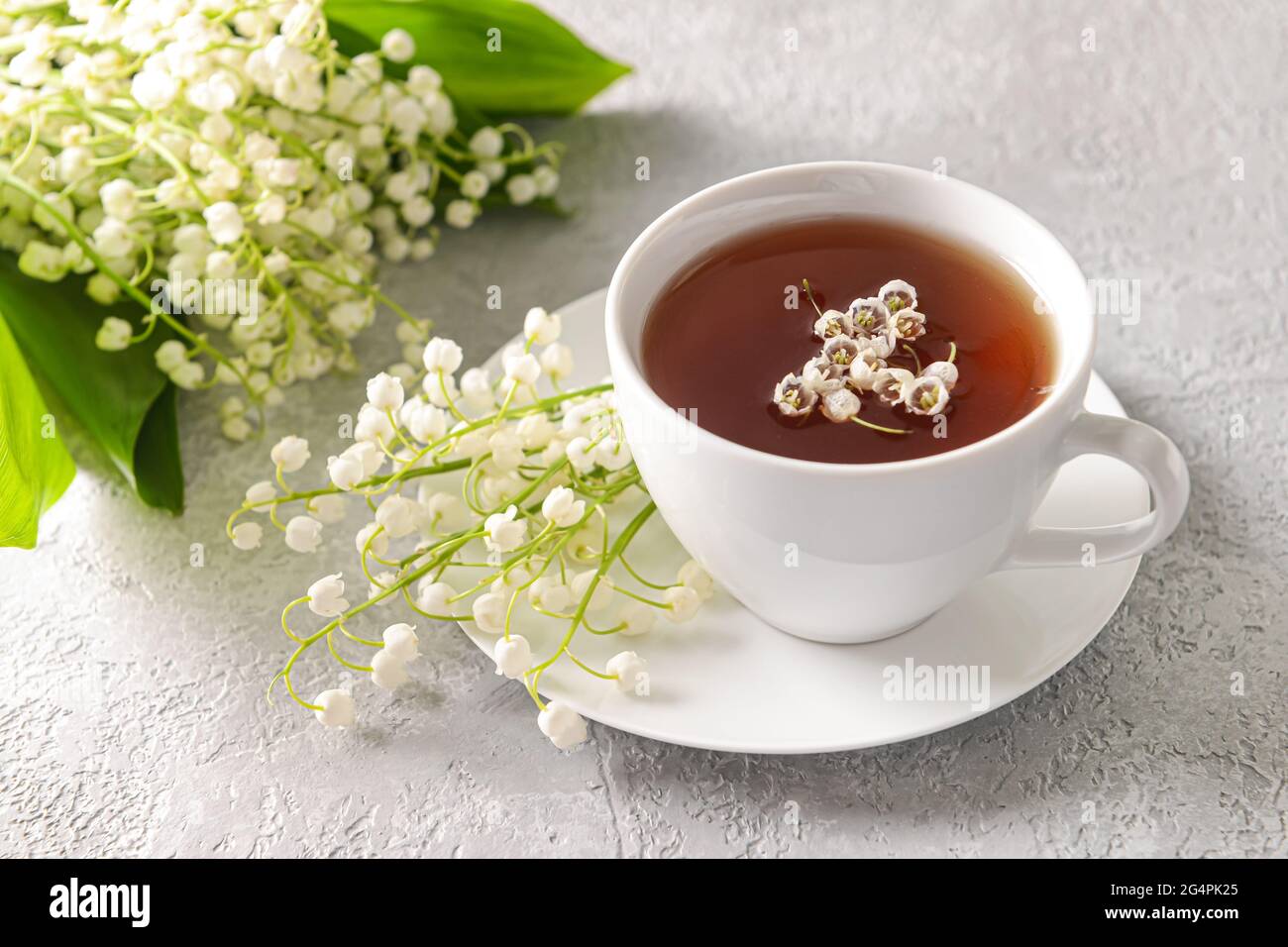 Beautiful lilyofthevalley flowers and cup of tea on light background