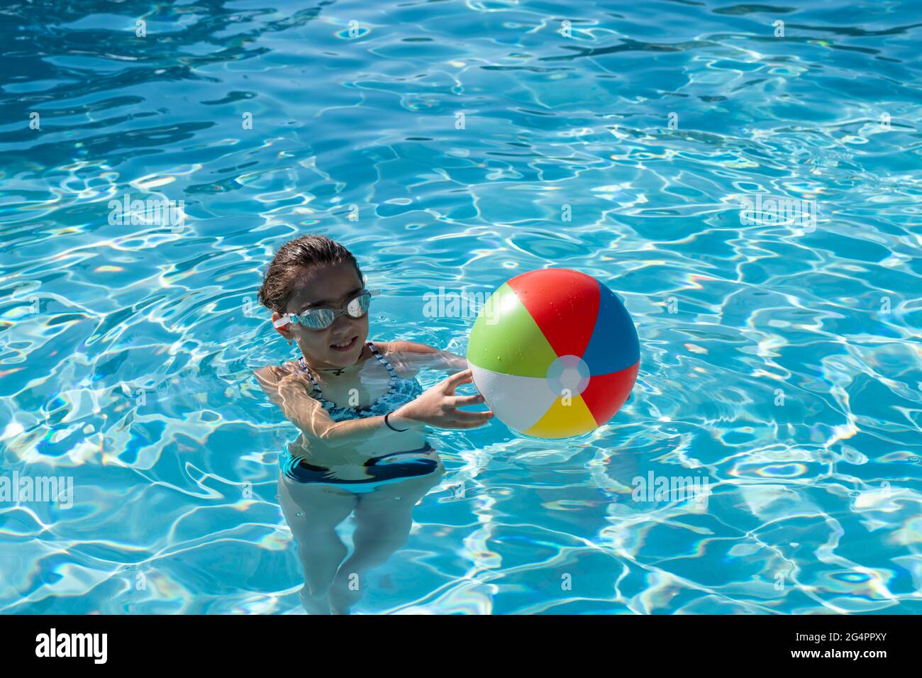 Young girl playing with beach ball in the swimming pool. Kid outdoor