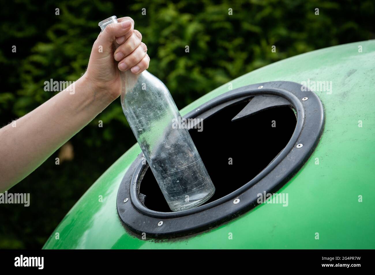 Throwing empty glass bottle into green recycle bin garbage container