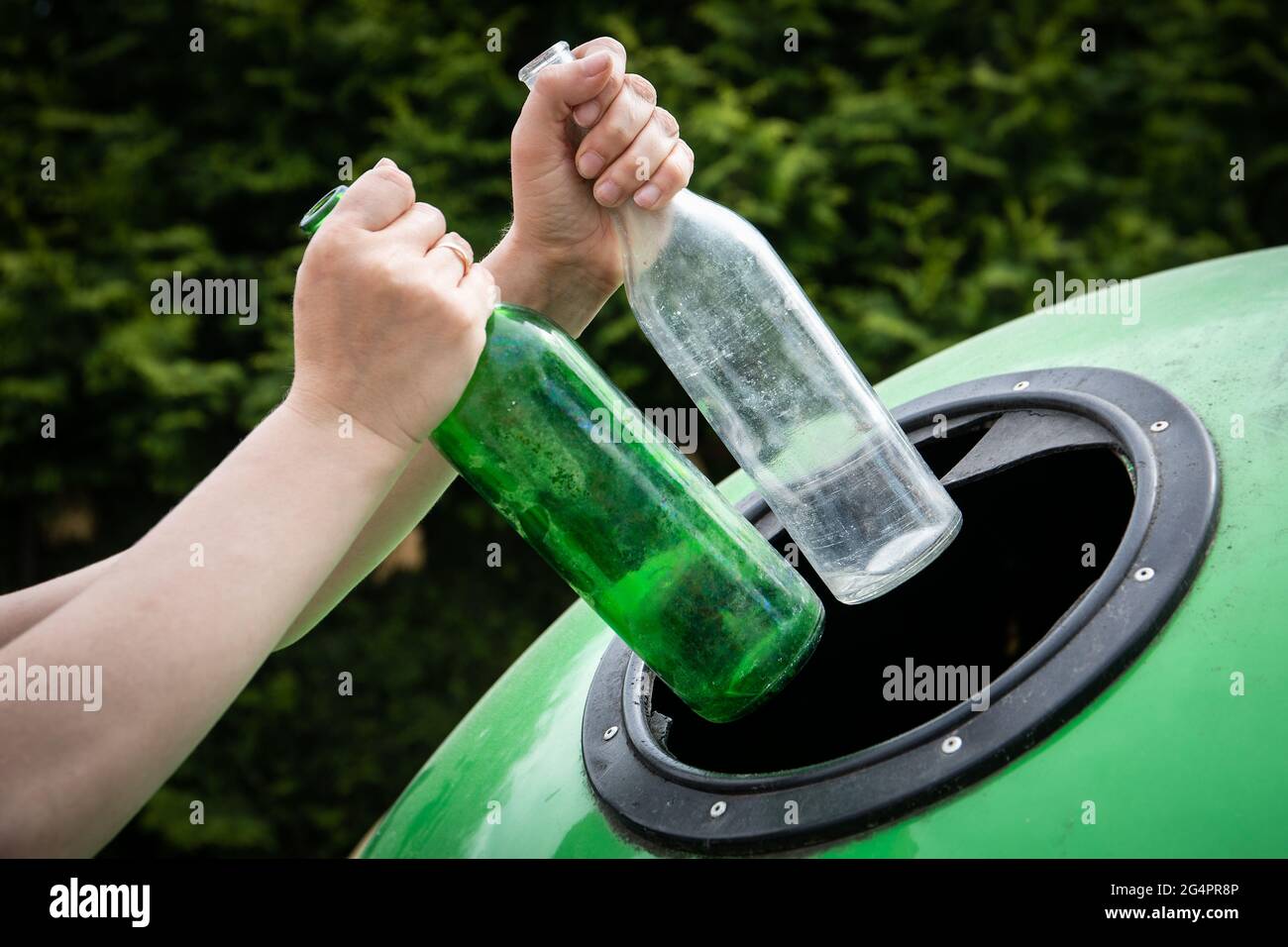 Throwing two empty glass bottle into green recycle bin garbage