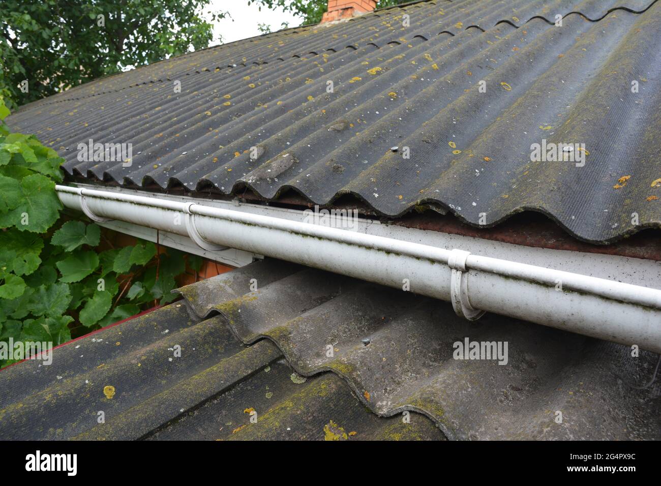 A close-up of an asbestos roof with a plastic roof gutter. An old corrugated asbestos roof. Stock Photo