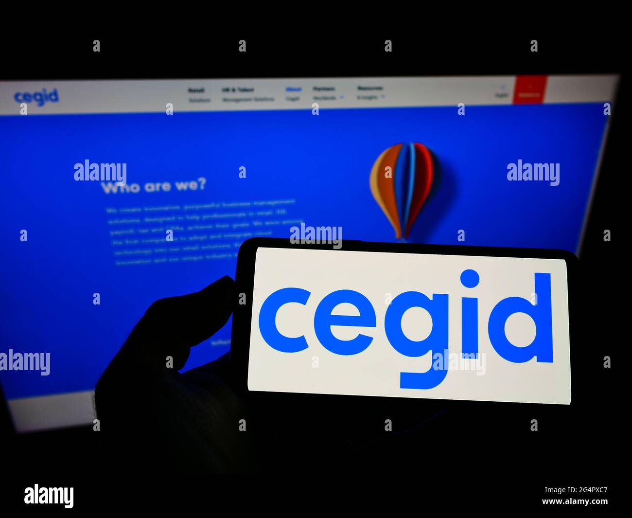 Person holding mobile phone with logo of French ERP software company Cegid SA on screen in front of business web page. Focus on phone display. Stock Photo