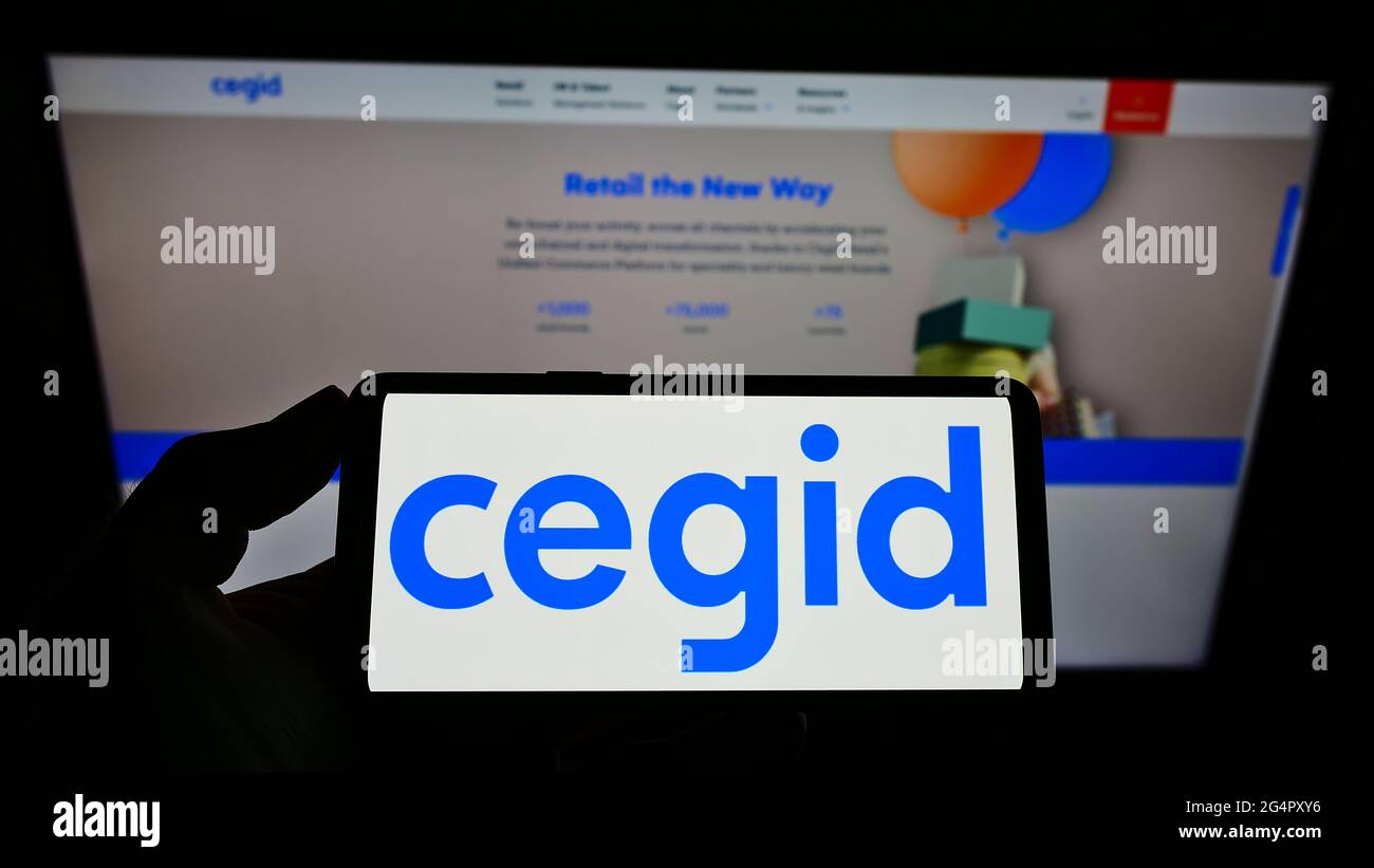 Person holding smartphone with logo of French ERP software company Cegid SA on screen in front of website. Focus on phone display. Stock Photo