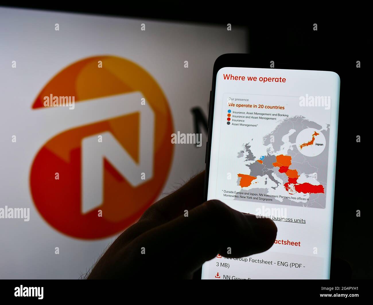 Person holding smartphone with webpage of Dutch insurance company NN Group N.V. on screen in front of logo. Focus on center of phone display. Stock Photo