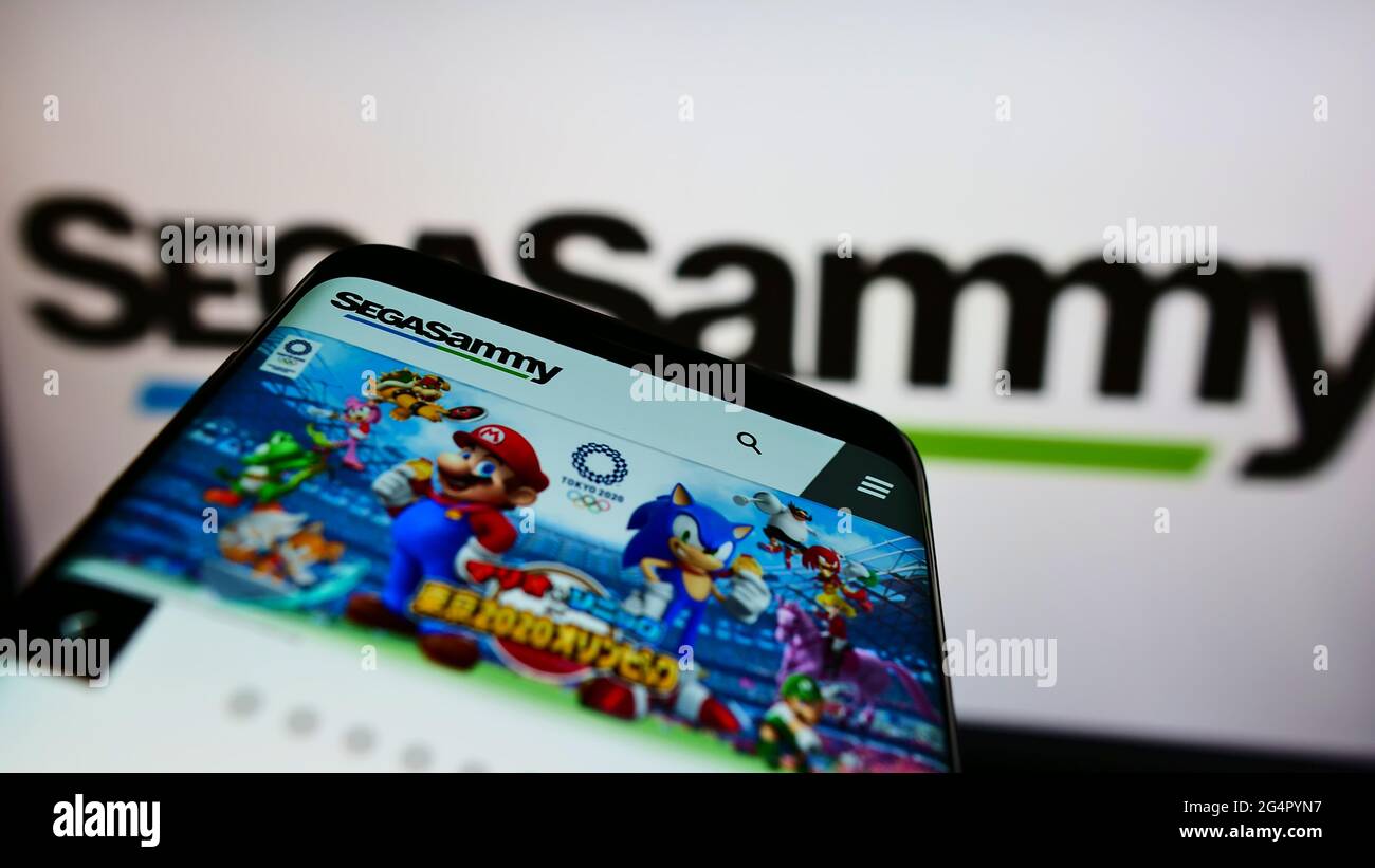 Smartphone with website of Japanese gaming company Sega Sammy Holdings Inc. on screen in front of business logo. Focus on top-left of phone display. Stock Photo