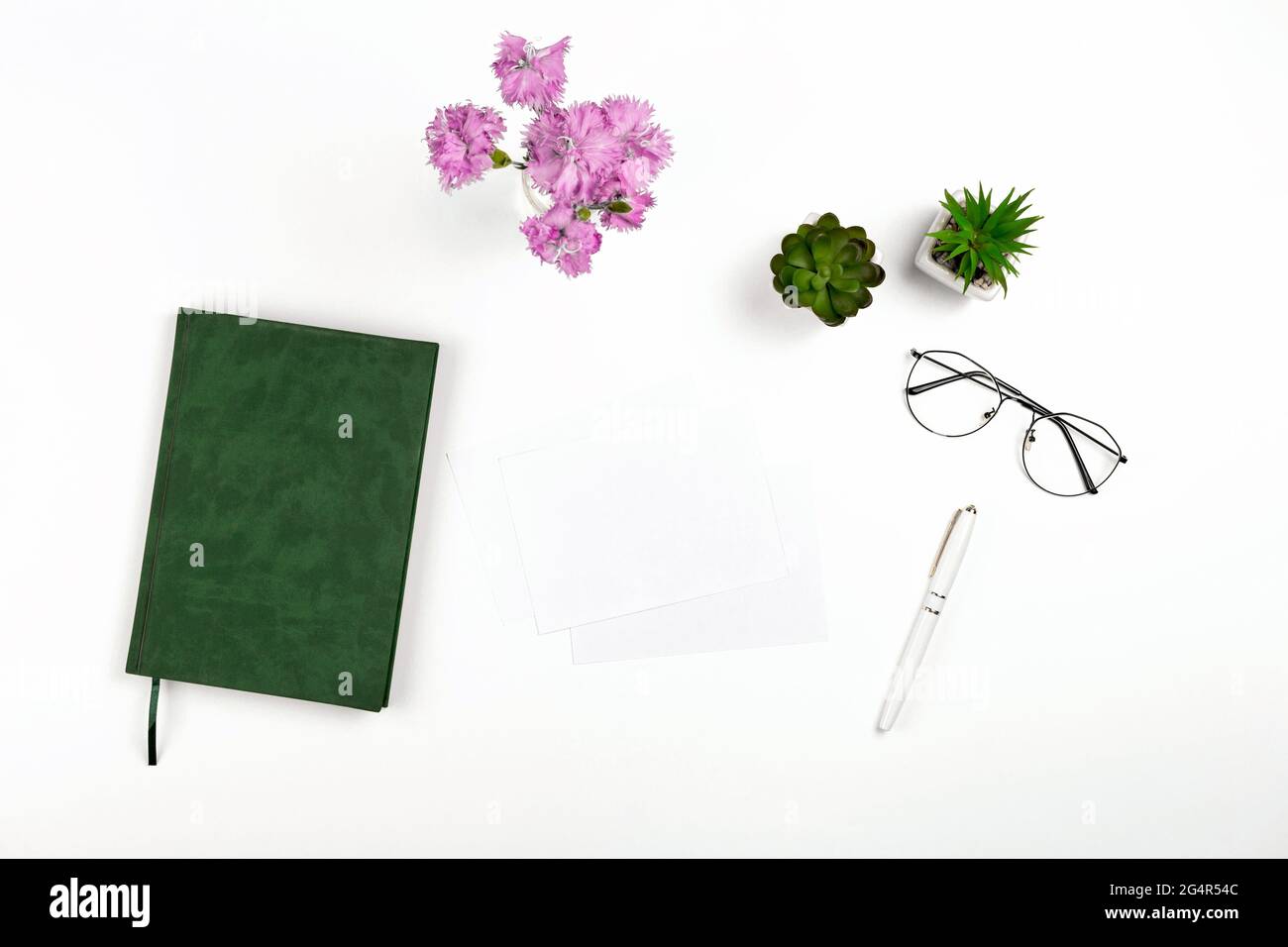 Light postcard mockup for design presentation on a white workplace with notebook, pen, glasses and flowers. Stock Photo
