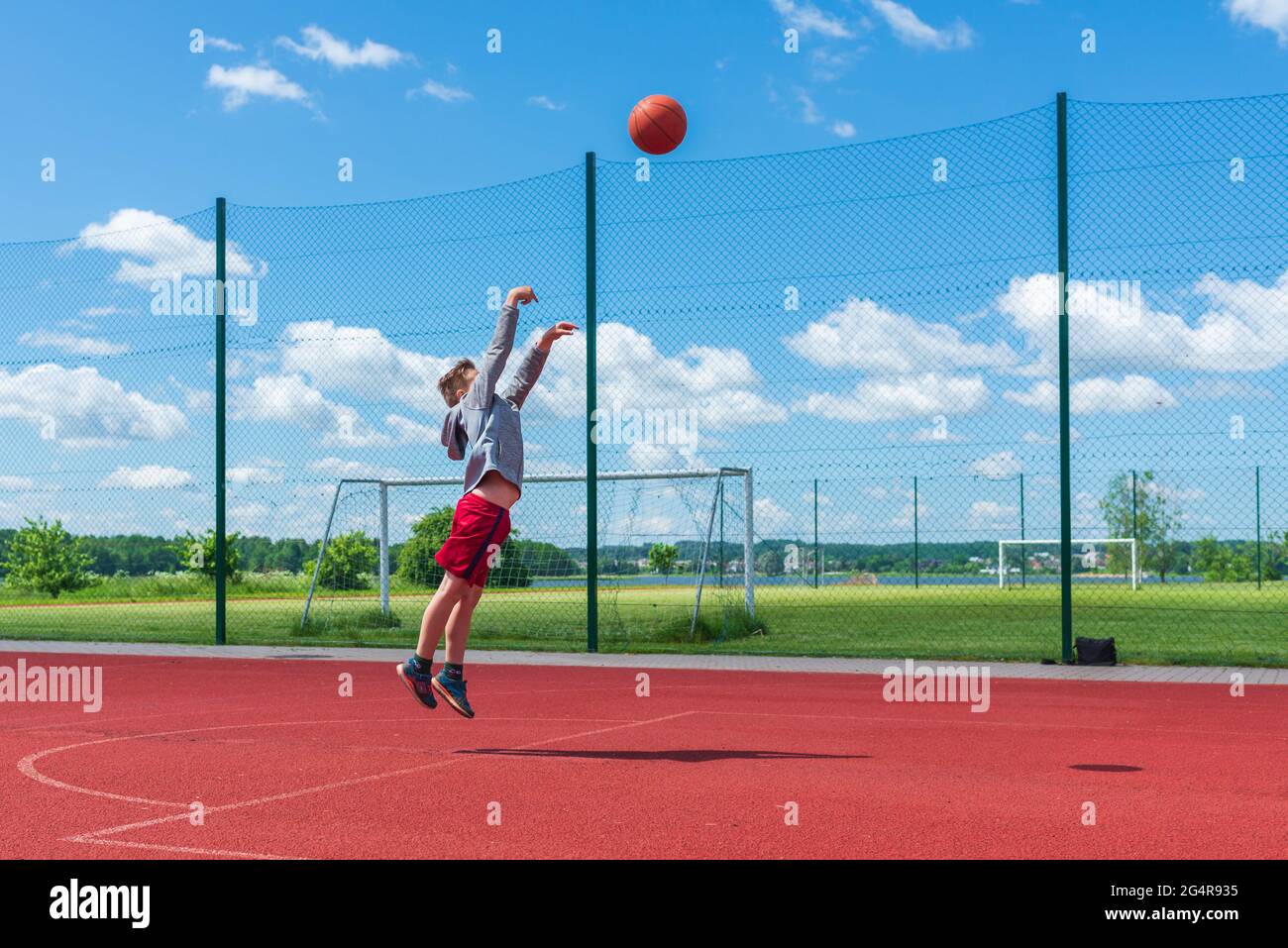 Attractive young boy shooting ball to the hoop at playground.cute young boy plays basketball on the playground in the summer warm day. Stock Photo