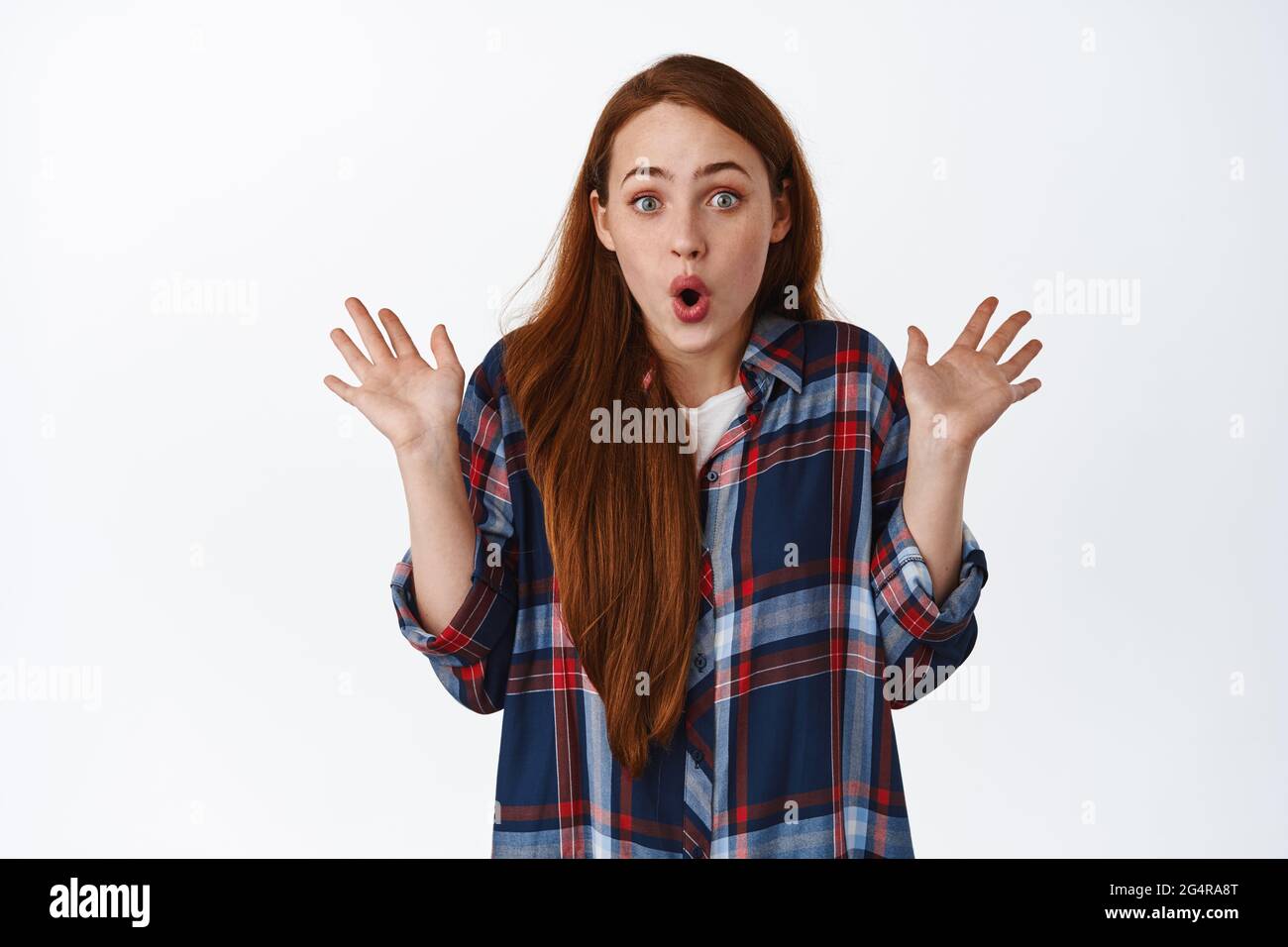 Impressed and surprised ginger girl, screams in awe, spread hands and looks amazed, hear awesome news, react to super good situation, white background Stock Photo