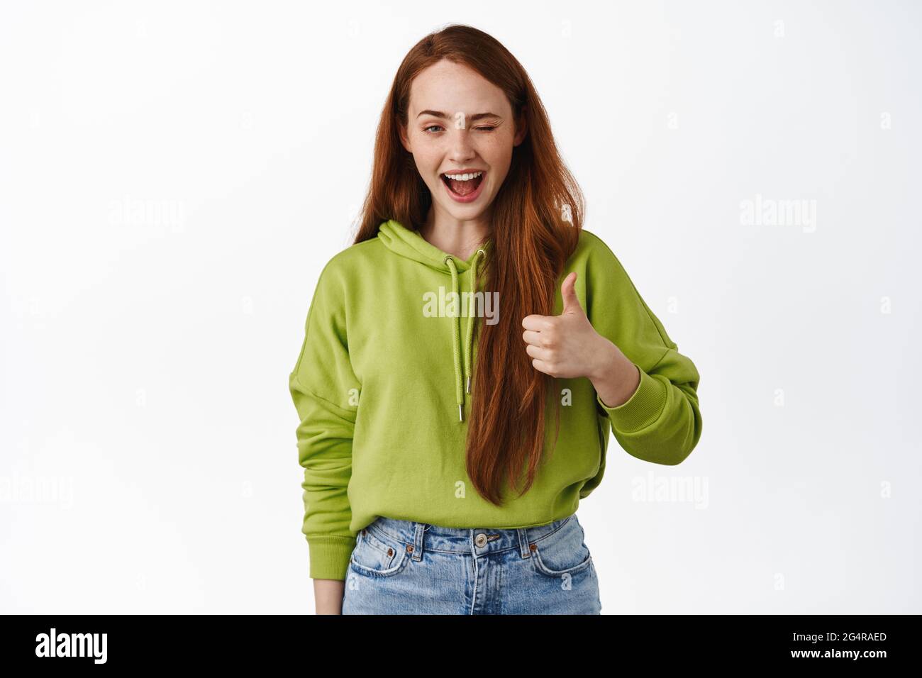 Cheerful girl student with long red hair, assure all god, no problem, make thumb up to praise great thing, say well done, confident in her choice Stock Photo