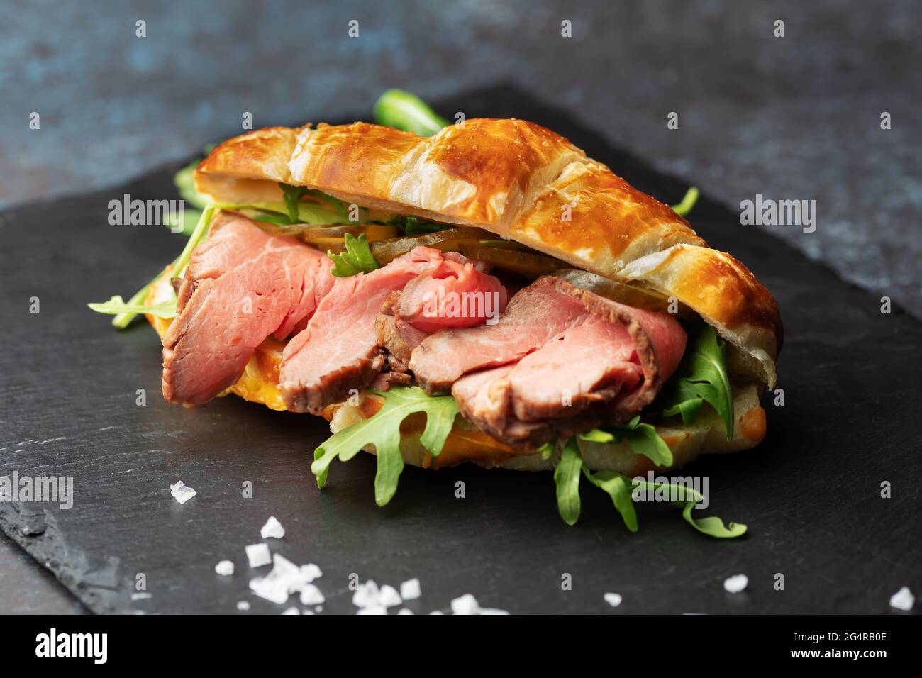 Fresh baked croissant sandwich with arugula and roast beef on a black