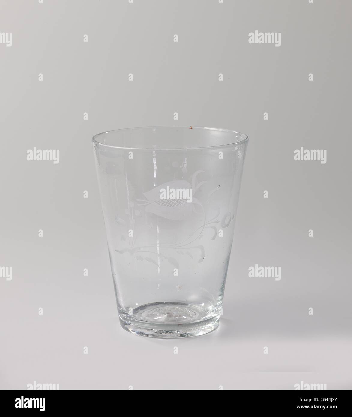 Cup with a flower. Cup of clear, colorless glass, conical, on which a very simple flower with the roulet cut. Stock Photo
