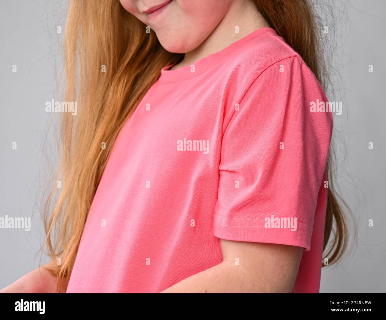 Close-up of red-haired kid girl pink t-shirt sleeve and chest. Side view. Summer clothing Stock Photo