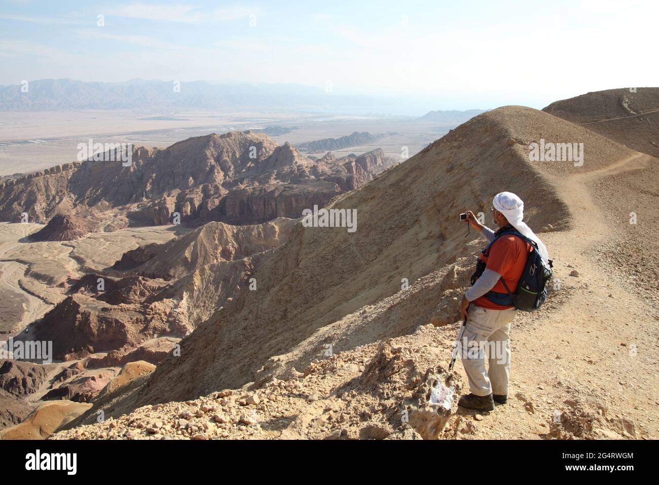 Hiker, senior adult (58) stands on Amram Heights photographing the Granite & Limestone Eilat Mountains, Arava Valley, Edomite Mts.& Red Sea by Eilat. Stock Photo