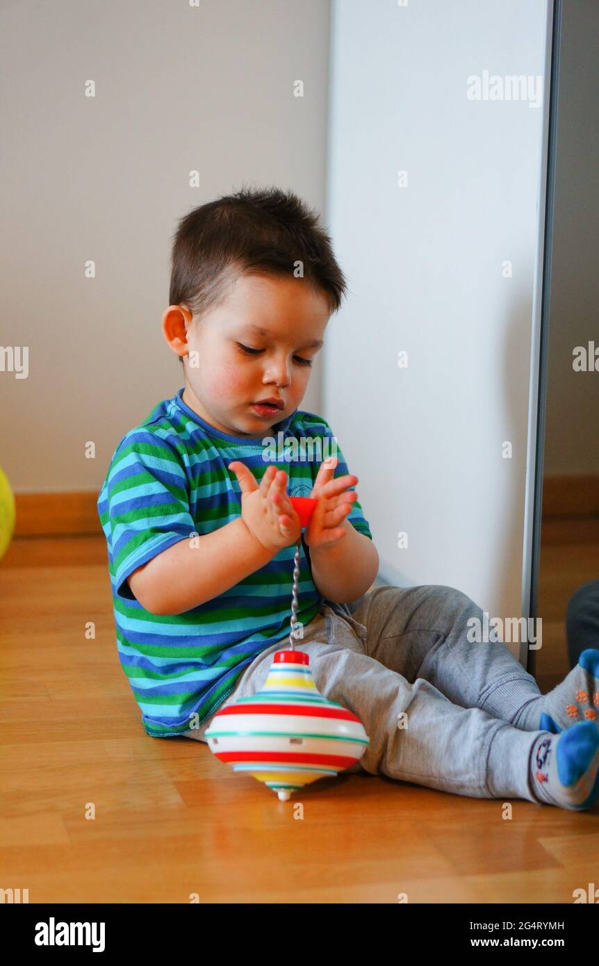 POZNAN, POLAND - Feb 21, 2016: Young boy playing with a spinning top toy on a wooden floor. Stock Photo