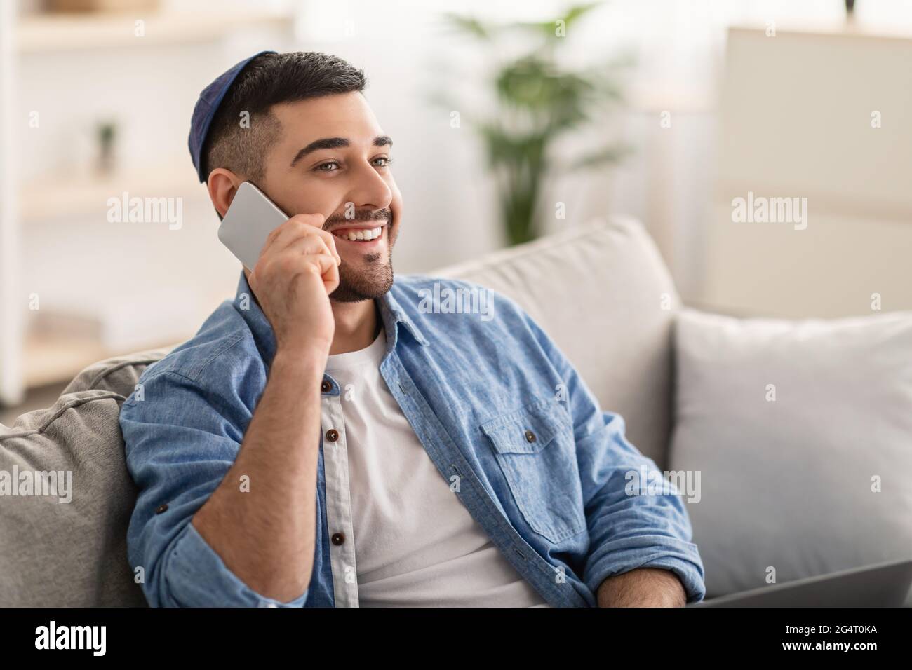 Phone Call Concept. Closeup portrait of smiling young jewish guy talking on smartphone with friends or family, sitting on confortable couch. Free copy Stock Photo