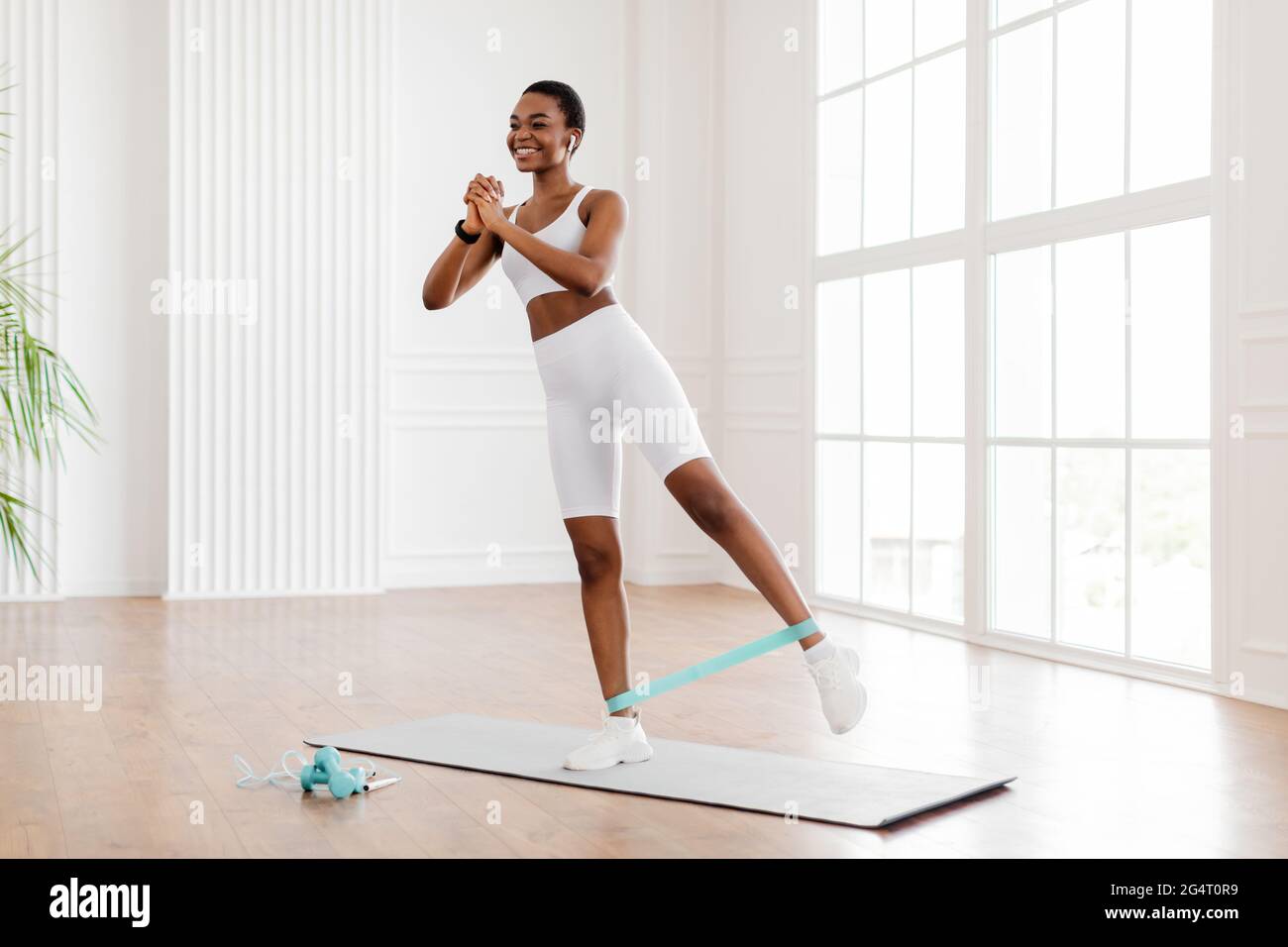 Full And Lower Body Workout. Happy Sporty African Woman Exercising With  Elastic Rubber Band Lifting And Kicking Leg Standing On Yoga Mat, Listening  To Stock Photo - Alamy