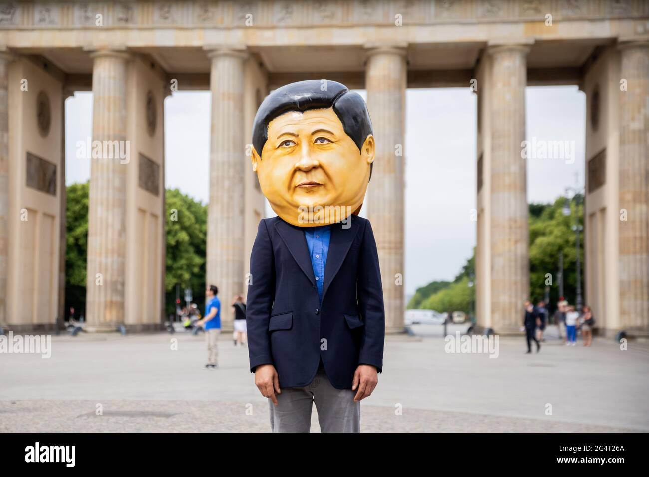 Berlin, Germany. 23rd June, 2021. A participant in a protest by several human rights organizations against the awarding of the 2022 Winter Olympics to Beijing stands in front of the Brandenburg Gate wearing a mask meant to represent Chinese President Xi Jinping. Credit: Christoph Soeder/dpa/Alamy Live News Stock Photo