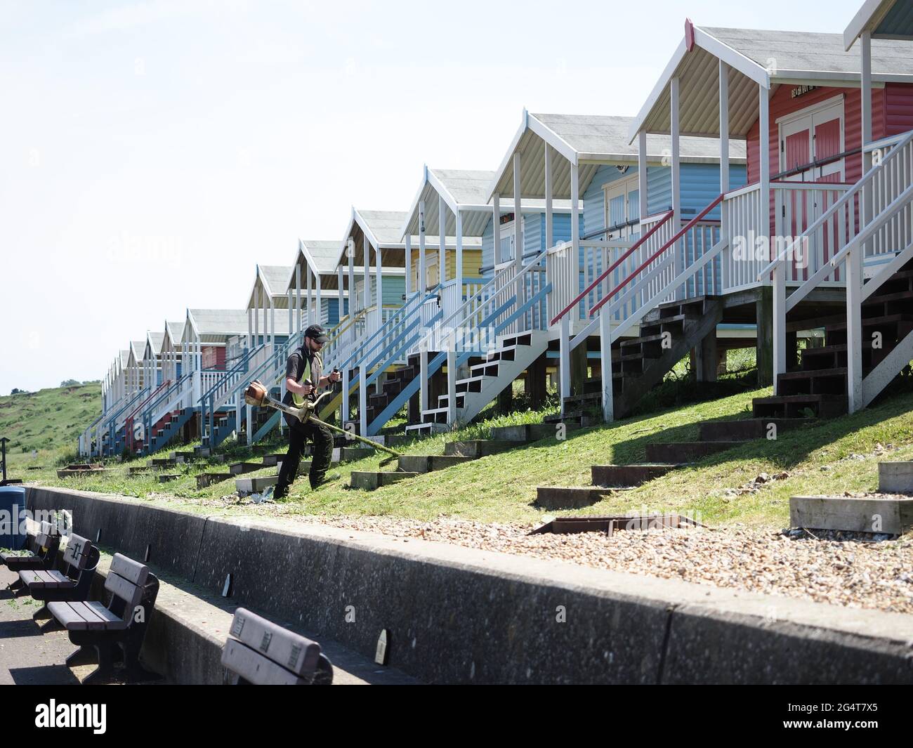 Minster on Sea, Kent, UK. 23rd June, 2021. UK Weather: a sunny & warm afternoon in  Minster on Sea, Kent. A council worker strims grass in front of beach huts ahead of forecast hot weather. Credit: James Bell/Alamy Live News Stock Photo