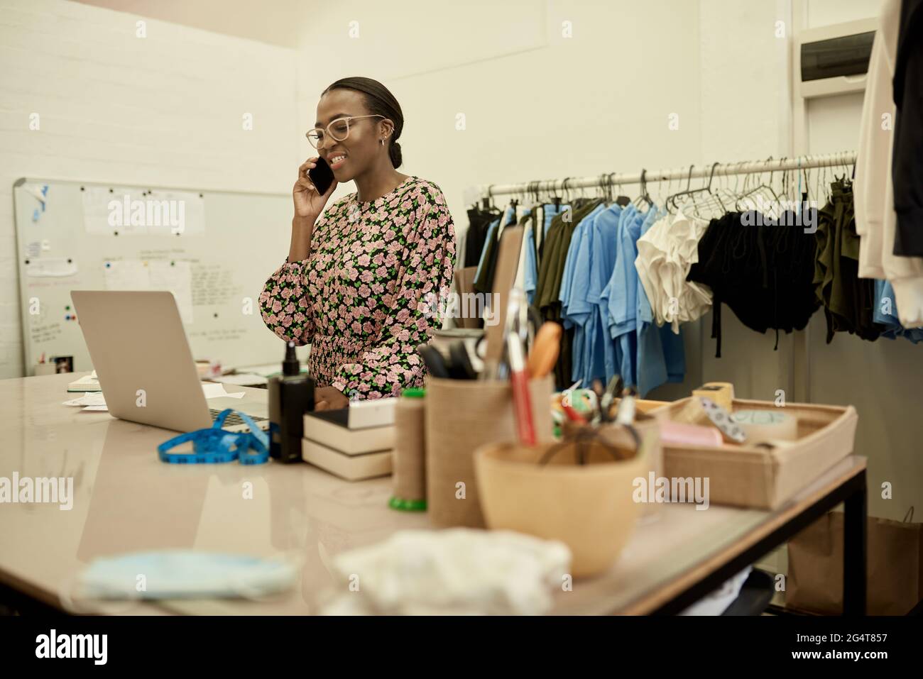Smiling African female fashion designer talking on the phone in her workshop Stock Photo