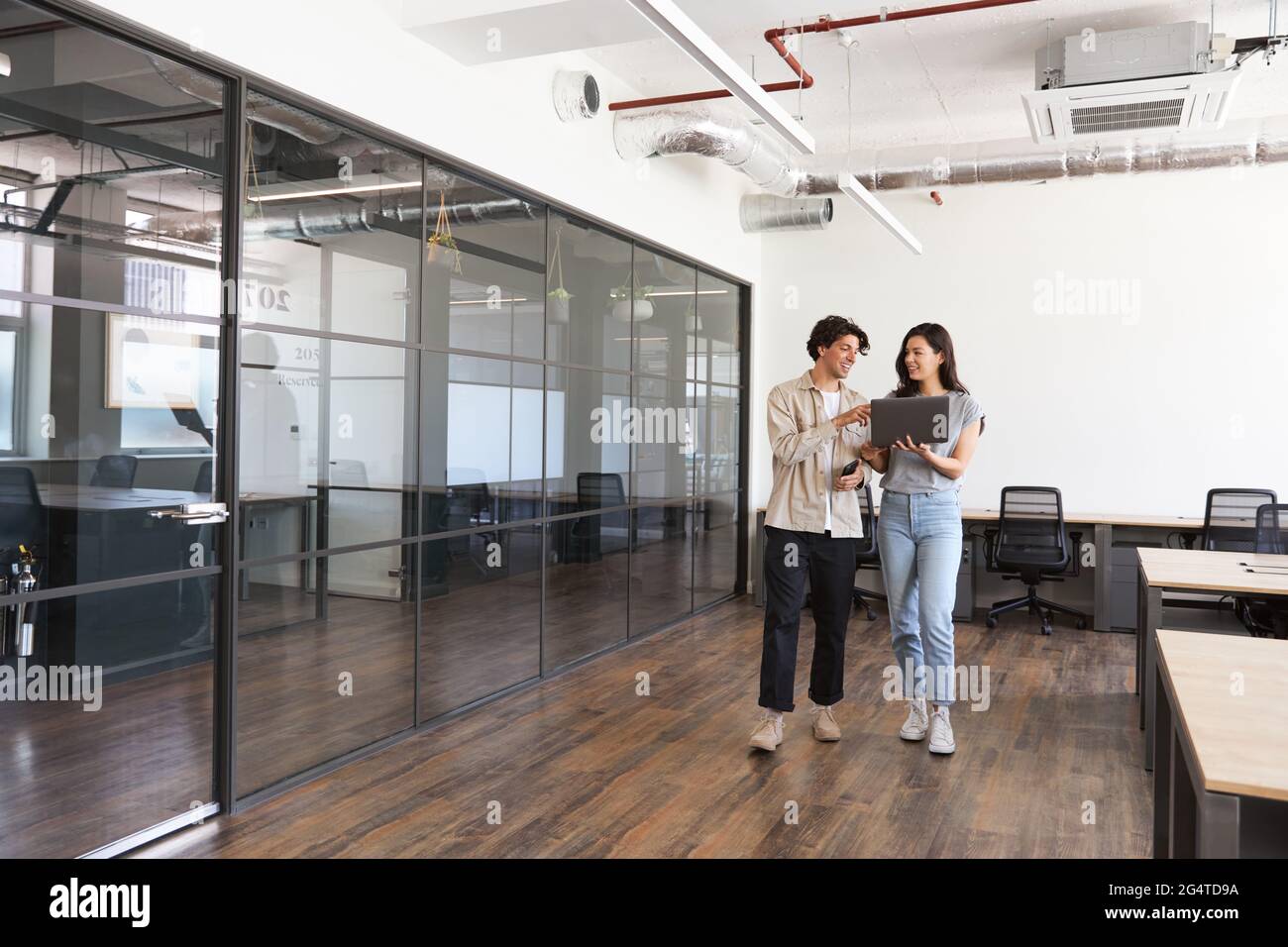 Casually dressed young man and woman working in modern open plan office ...