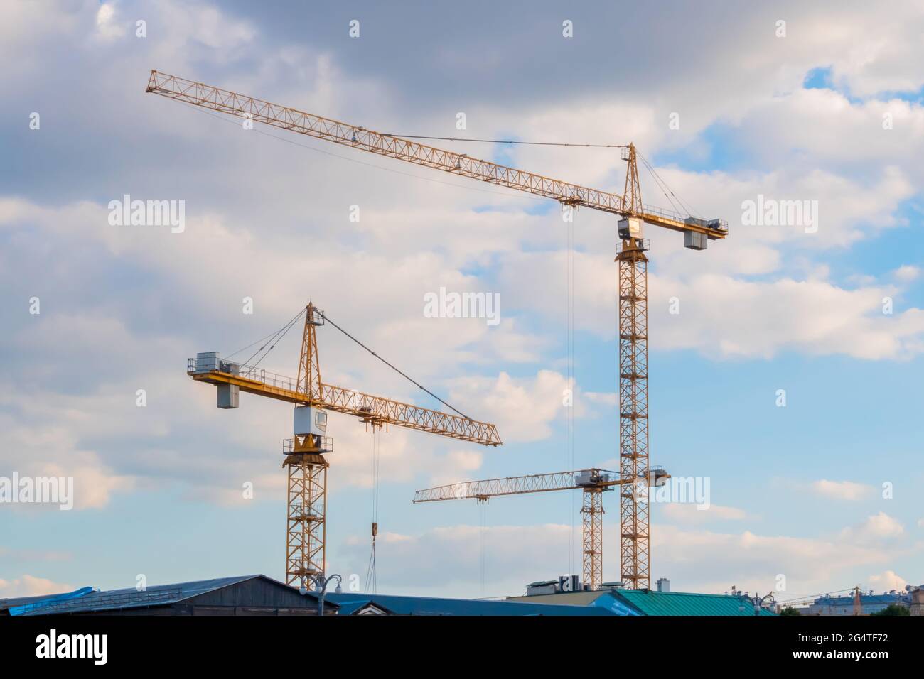 Three yellow tower construction cranes against cloudy sky Stock Photo
