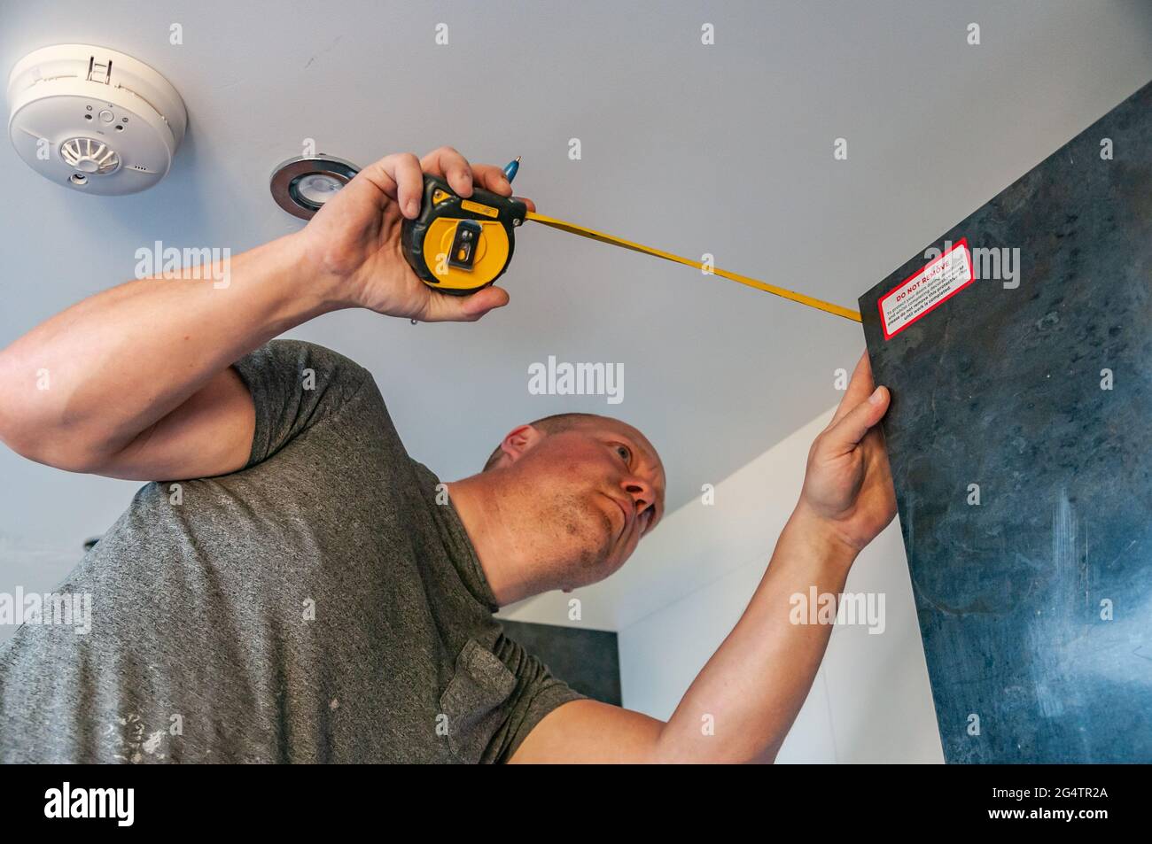 A kitchen fitter measures a wall-mounted kitchen cupboard Stock Photo