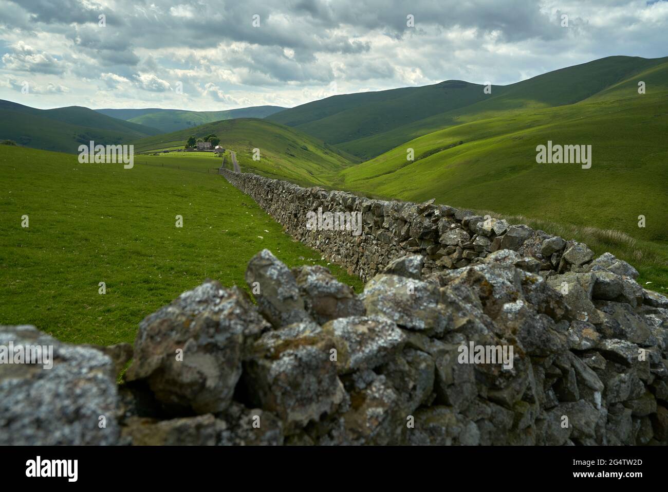 Remote Farm on hillside with stone wall and dramatic summer sky in the Scottish Borders. Unclassified road off the B 6399 Stock Photo