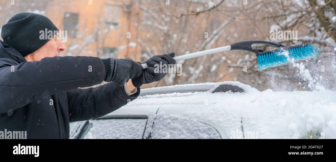 adult male removing snow from car roof with brush in winter season