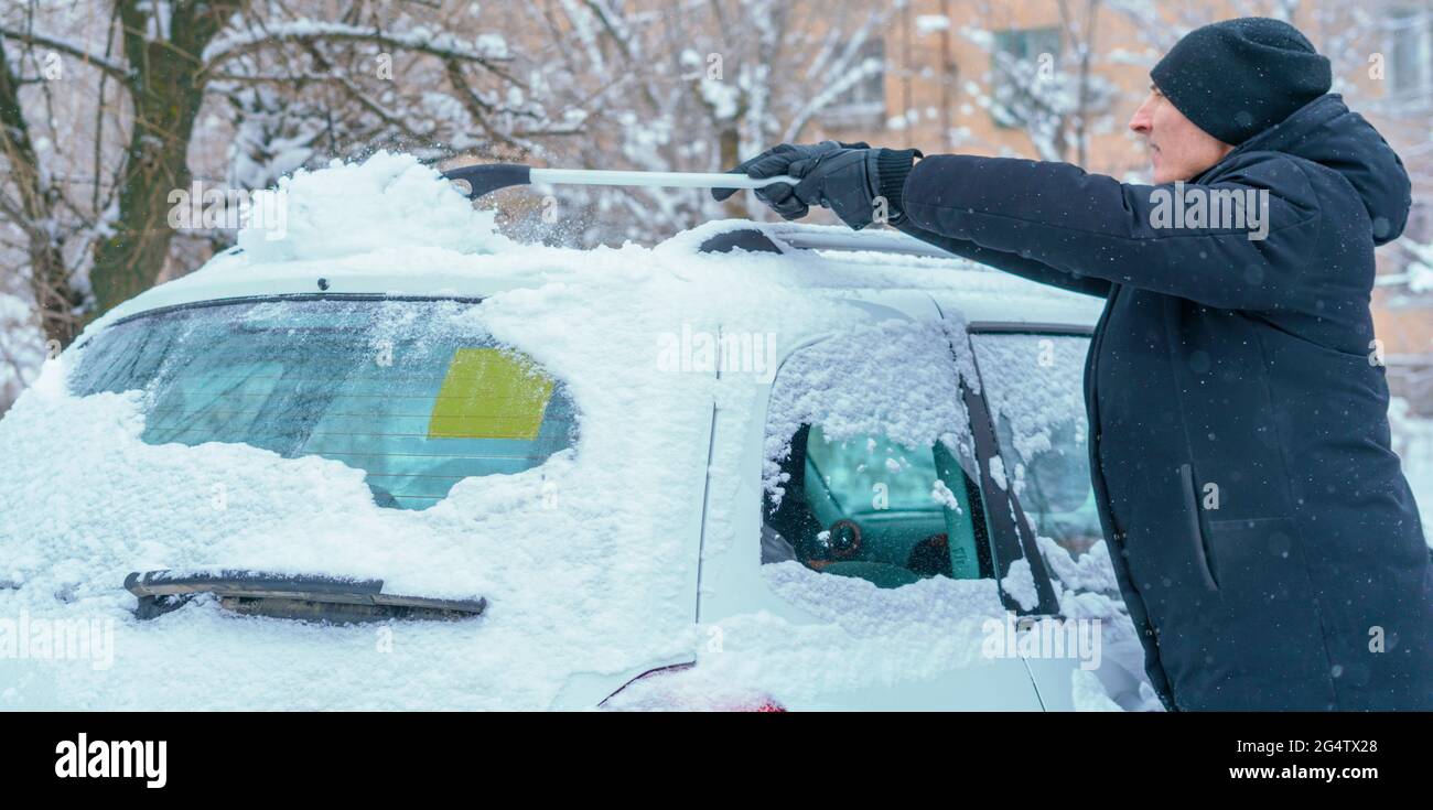 adult male removing snow from car roof with brush in winter season